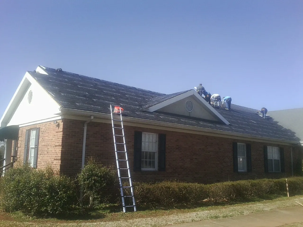 Crew tearing shingles off a brick ranch roof with a ladder set — Metal Roof Repair work by our crew in Waterport