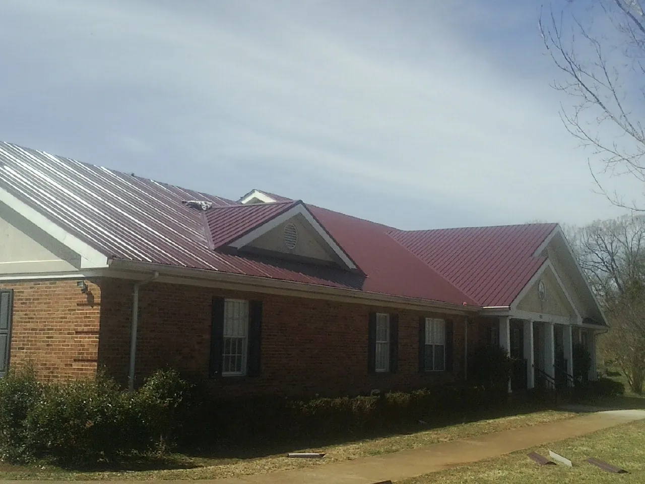 Red metal roof with gabled entries on a long brick building, from a Hail Damage Roof Repair job in Waterport