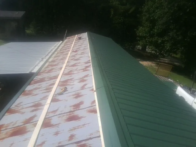Old rusted panels beside newly installed green metal roofing — Wind Damage Roof Repair by Roofing Brothers in Waterport
