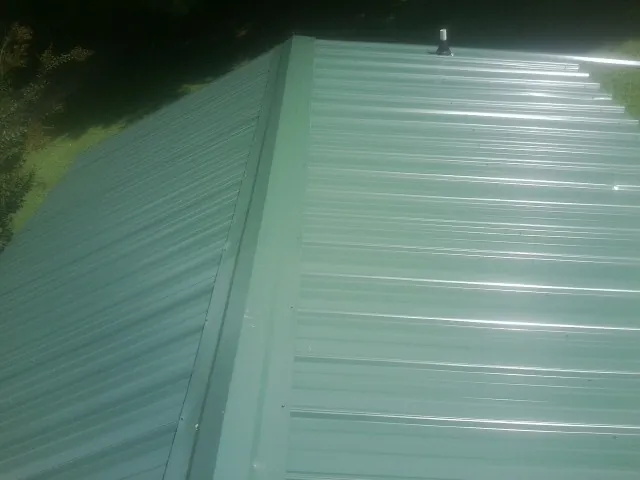 New green metal panels meeting at the ridge of a roof — Flat Roof Repair work by our crew in Waterport
