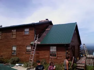 Green metal roof going on a two story log home with ladders set in Waterport