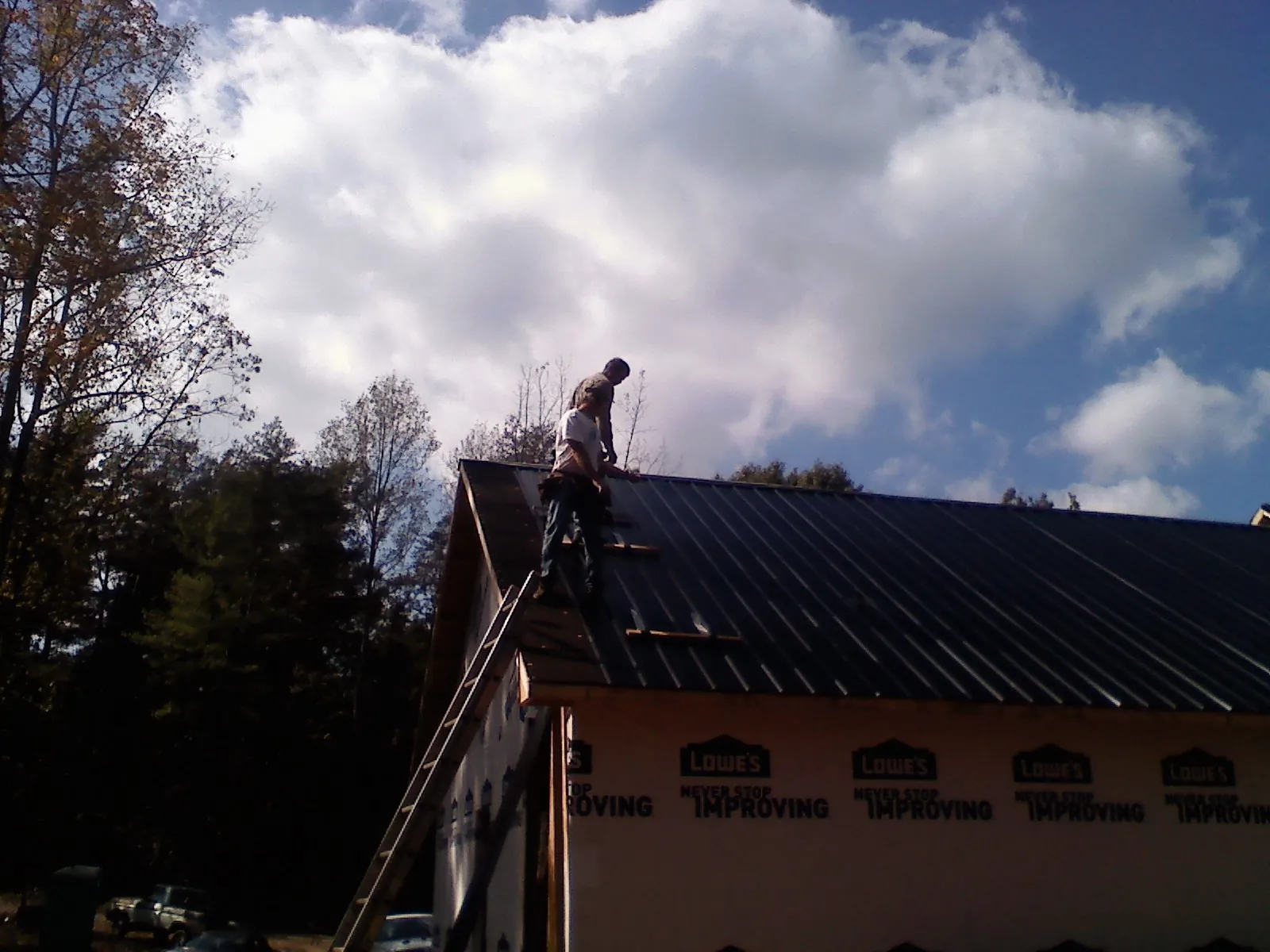 Roofer fastening dark metal panels high against a cloudy sky, from a Roof Inspection job in Waterport