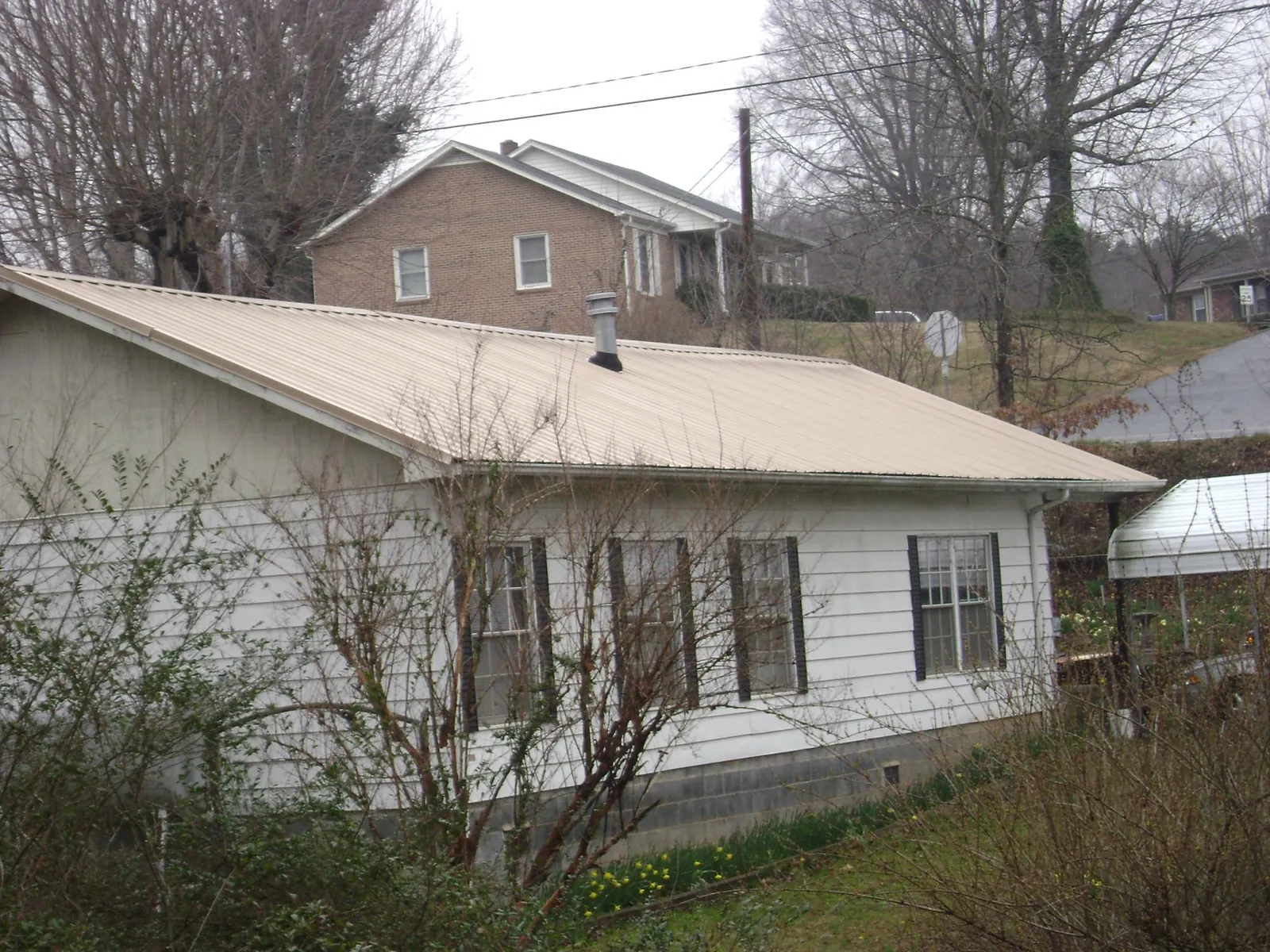 Tan metal roof on a white sided house set into a hillside — Commercial Roofing by Roofing Brothers in Waterport