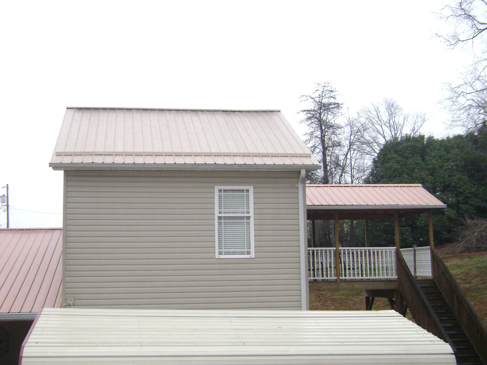 Tan metal roofs on a two story addition and attached porch, from a Roof Replacement job in Waterport